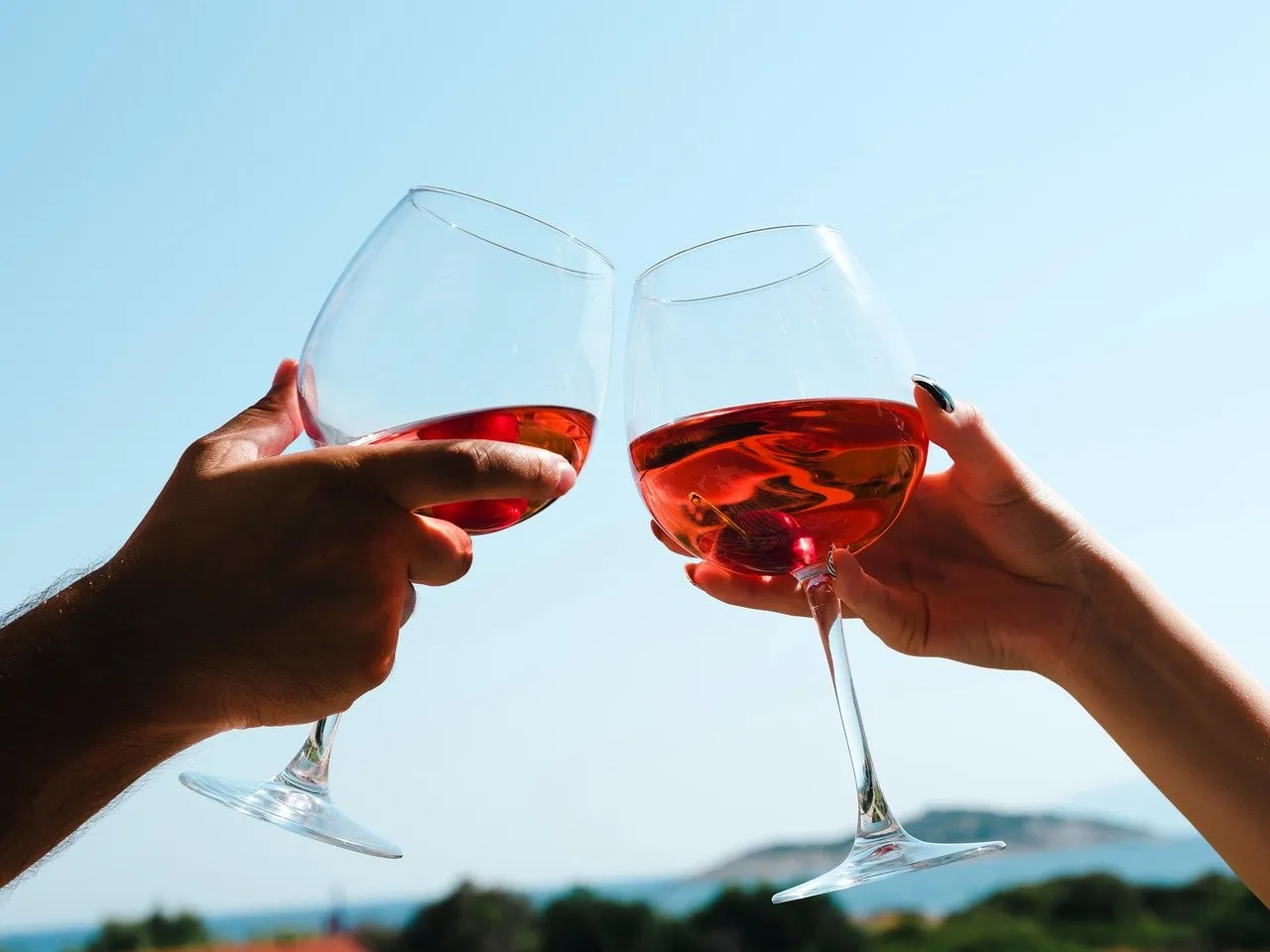 Two glasses of rosé raised in a toast against a clear blue sky and sea