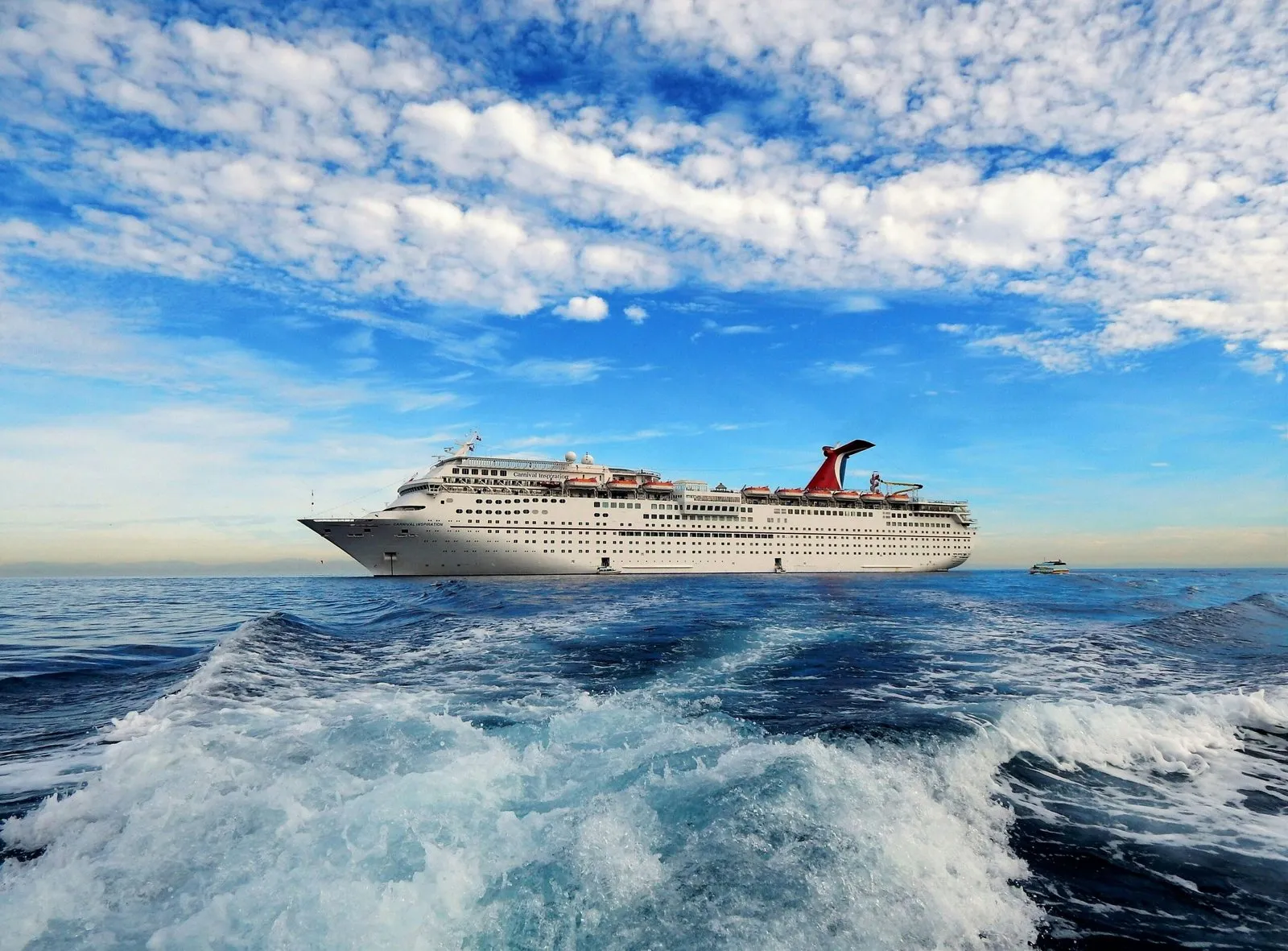 A cruise ship on a bright, cloud-flecked day at sea