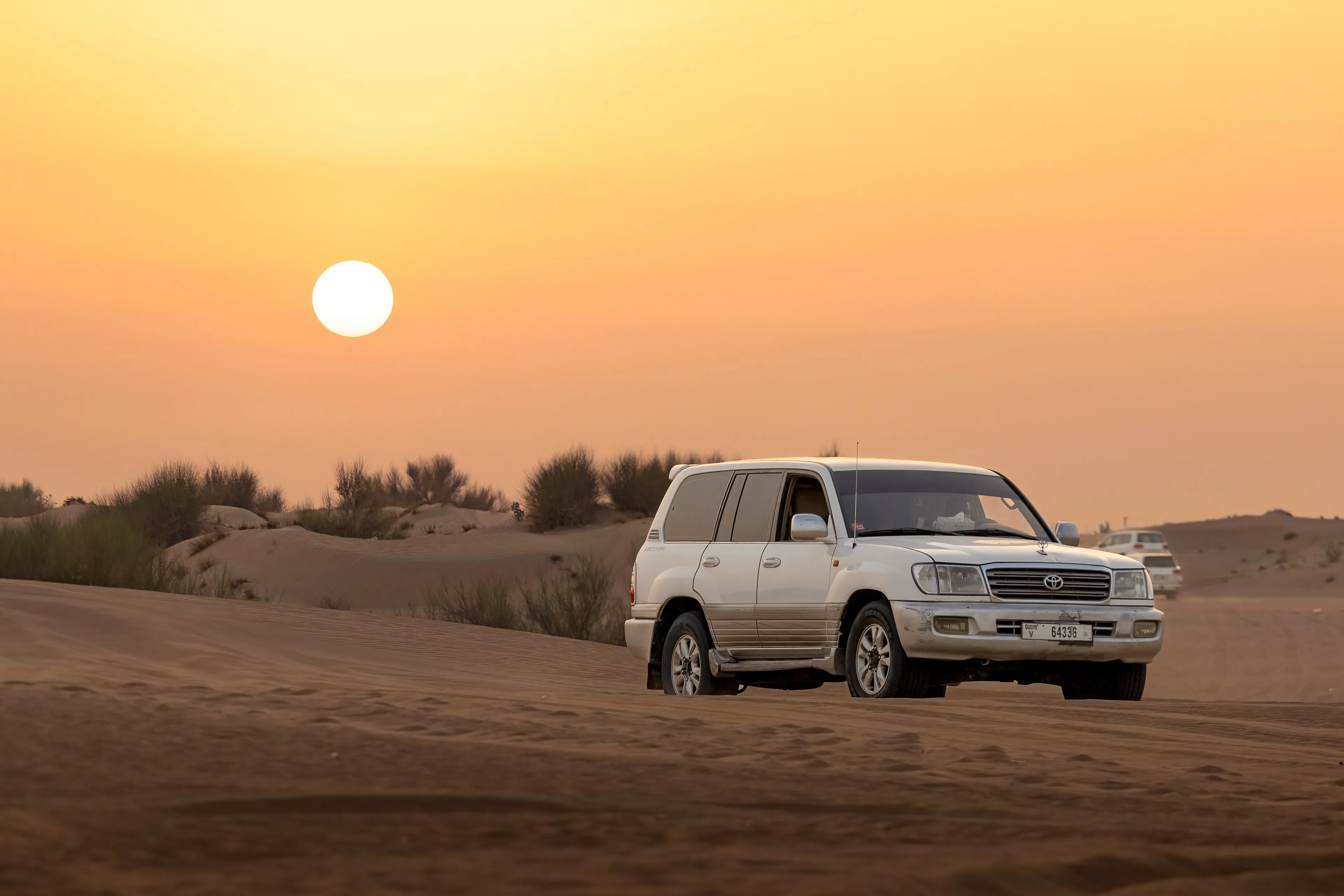 A four-wheel-drive vehicle crossing the dunes outside Dubai as the sun sets