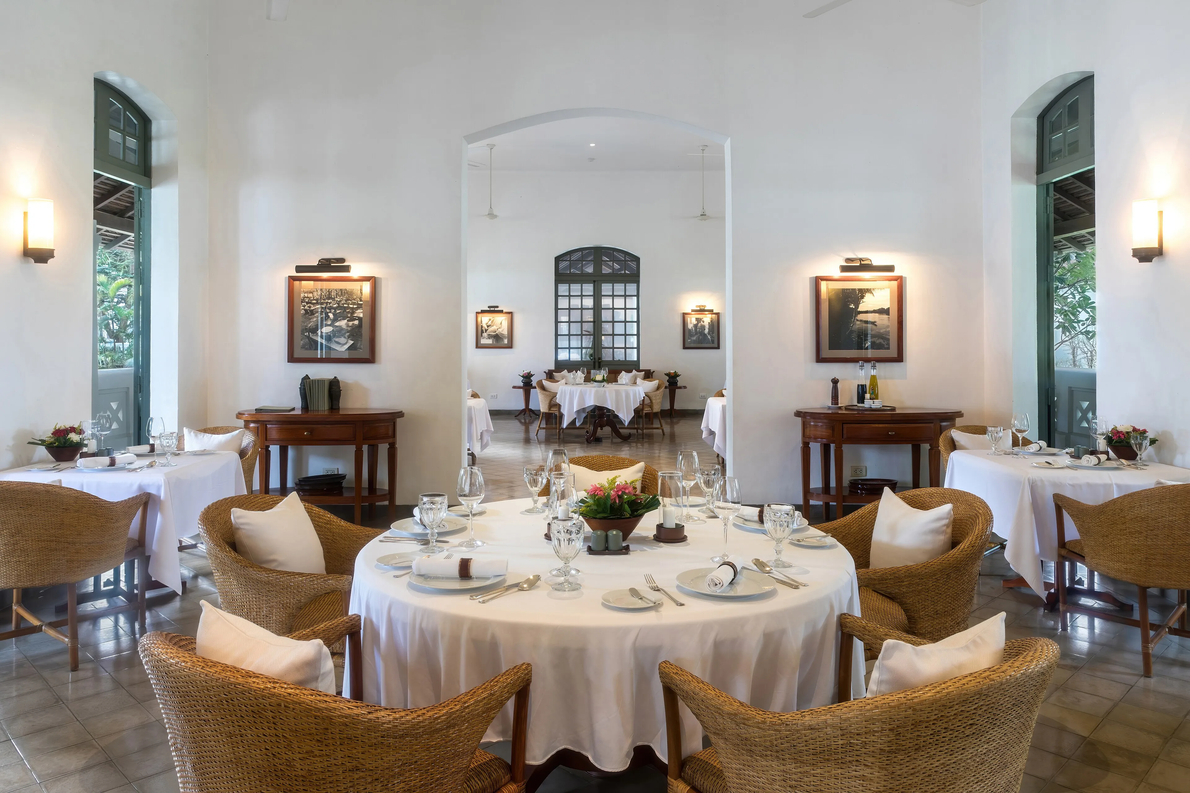 Tables laid with white linen and ringed by wicker armchairs in the airy, white-walled dining room of a luxury hotel