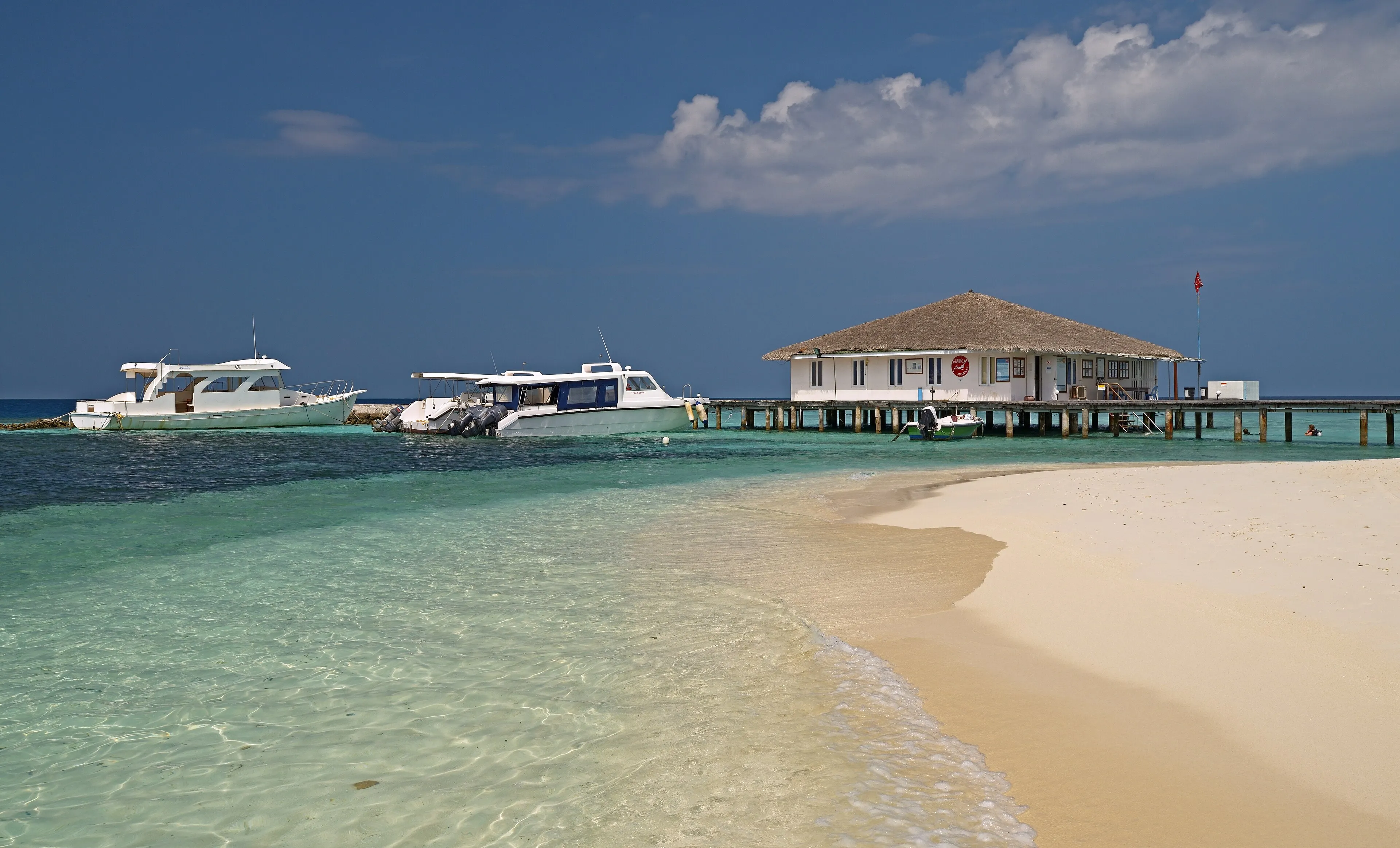 Boats moored in clear turquoise water beside a Maldivian island