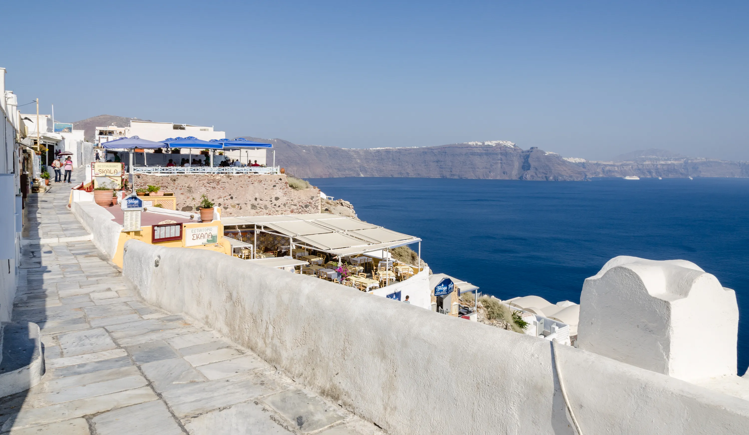 A whitewashed path along the caldera rim in Oia, Santorini, above the deep blue Aegean