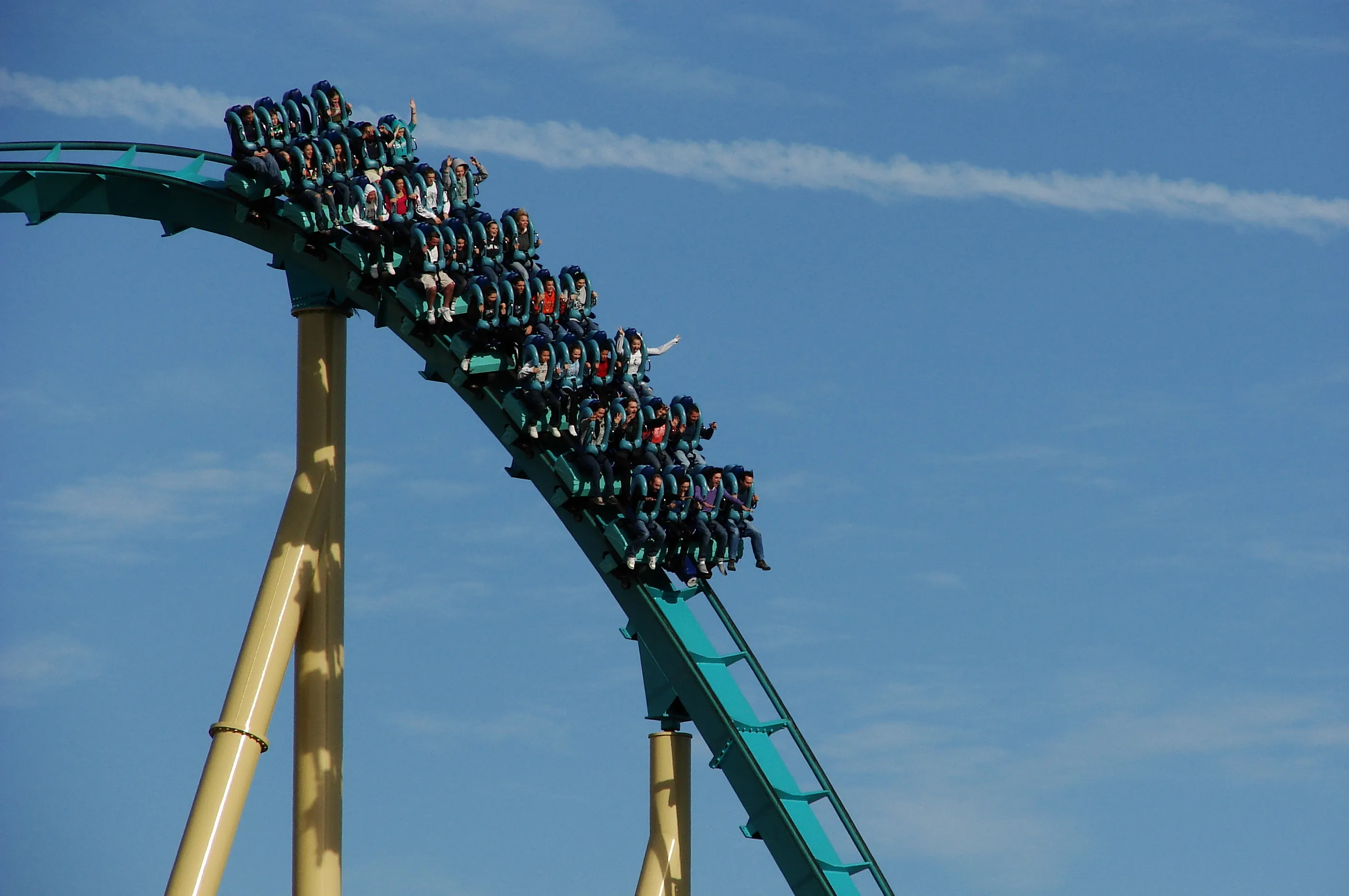 A roller coaster train full of riders, some with arms raised, tipping over into a drop against a blue sky at SeaWorld Orlando