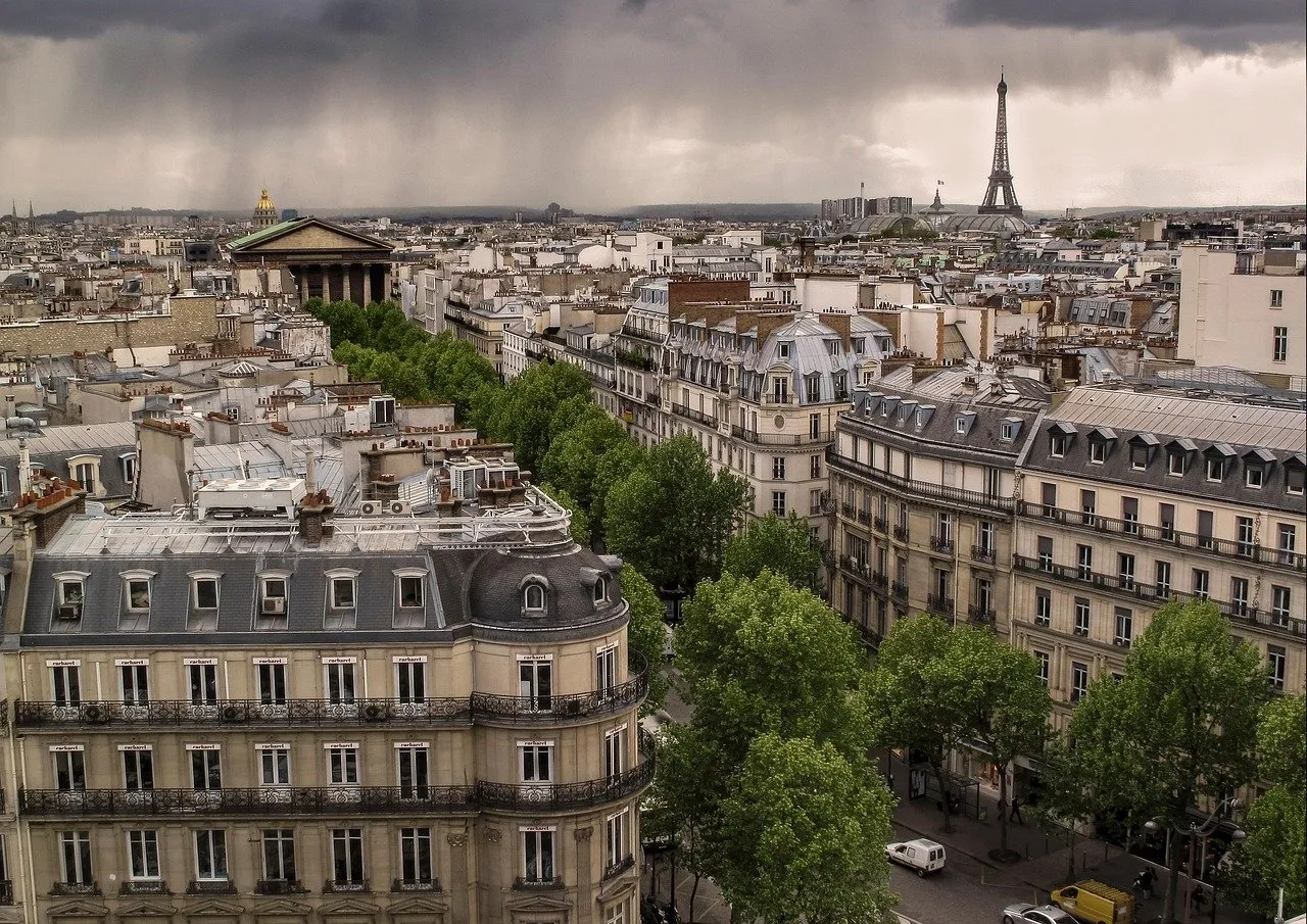 Paris rooftops beneath a dramatic sky with the Eiffel Tower in the distance