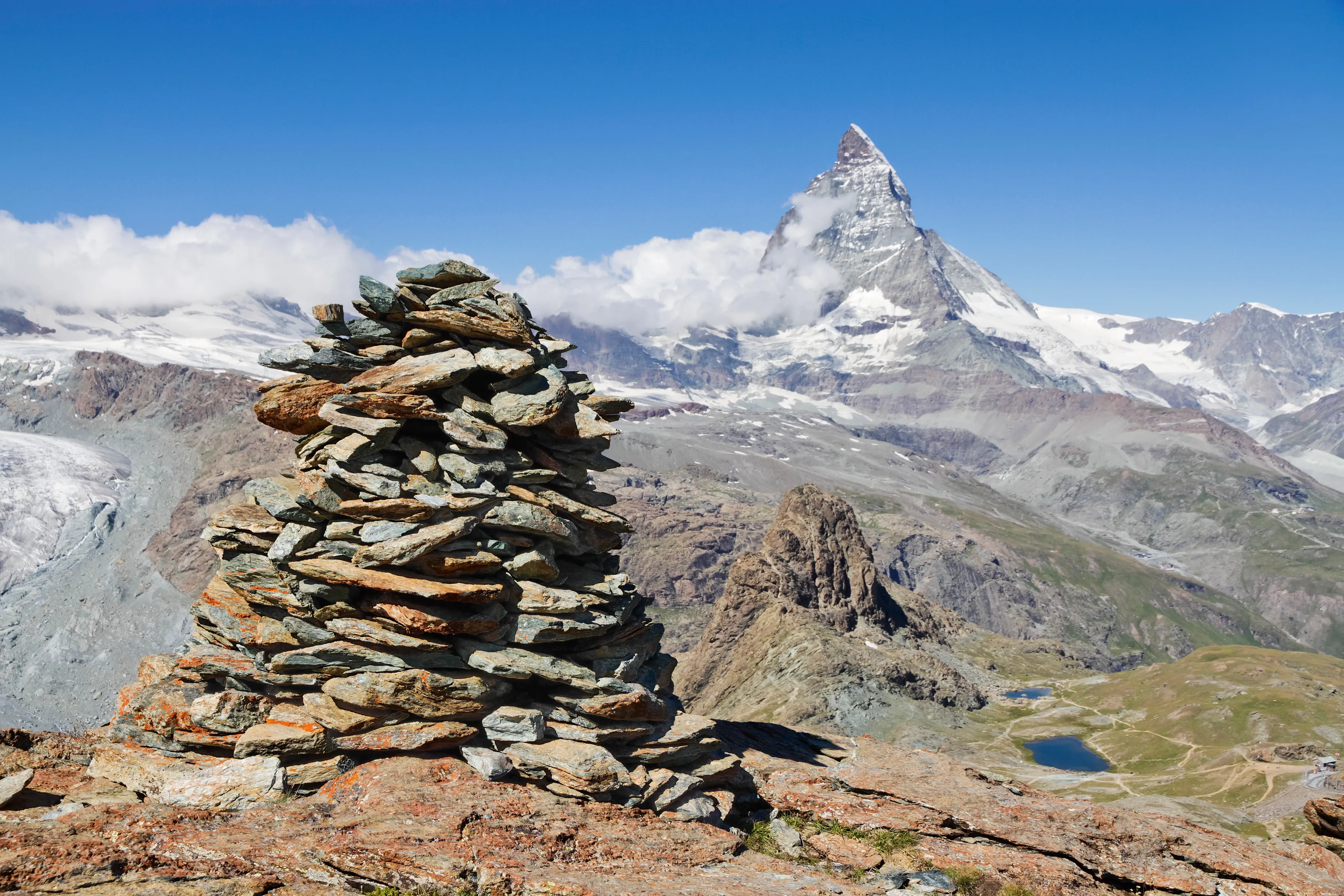 A stone cairn on the Gornergrat, with the Matterhorn rising beyond glaciers and small alpine lakes